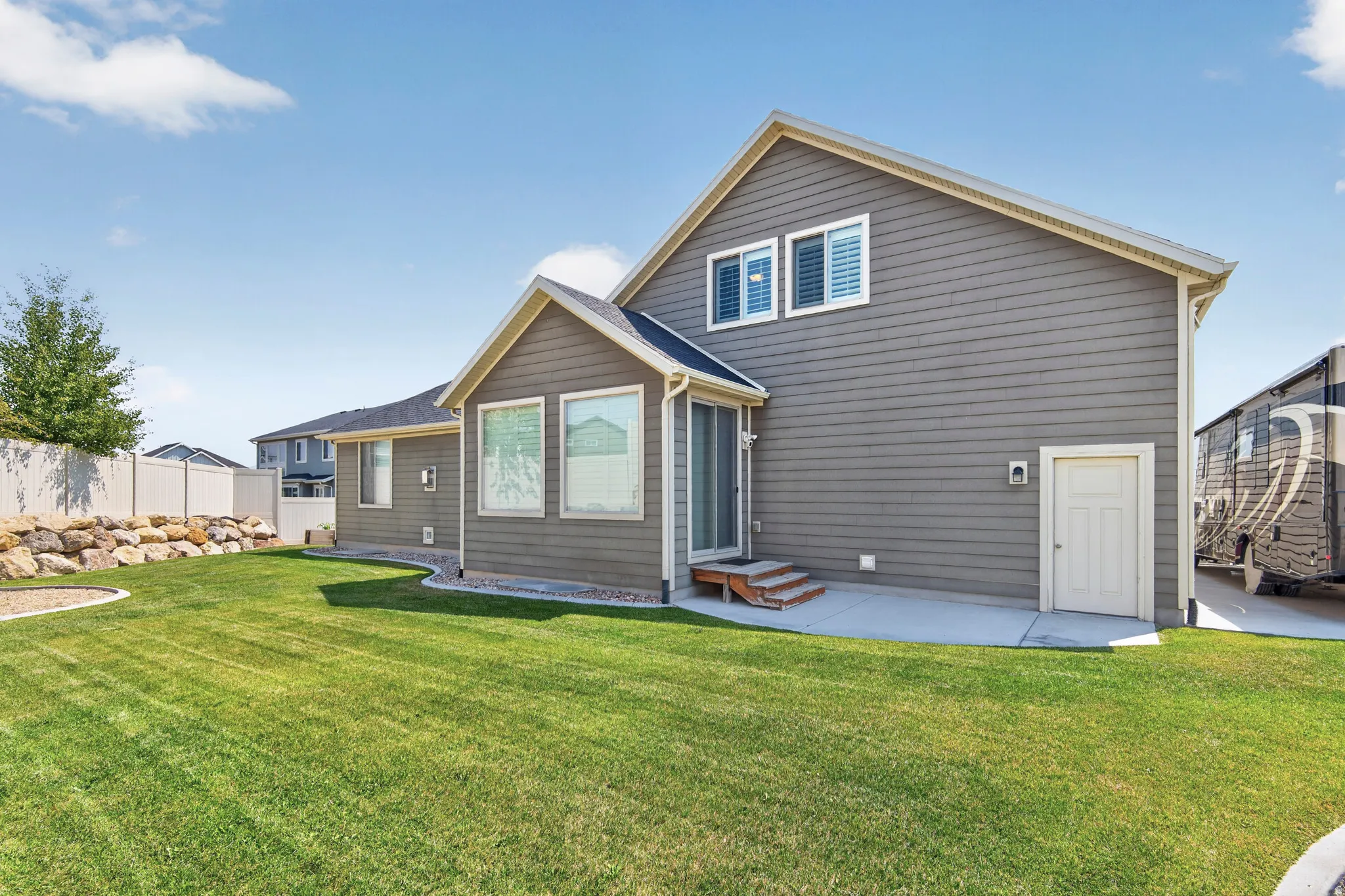Expansive green lawn with a rock retaining wall and a white privacy fence
