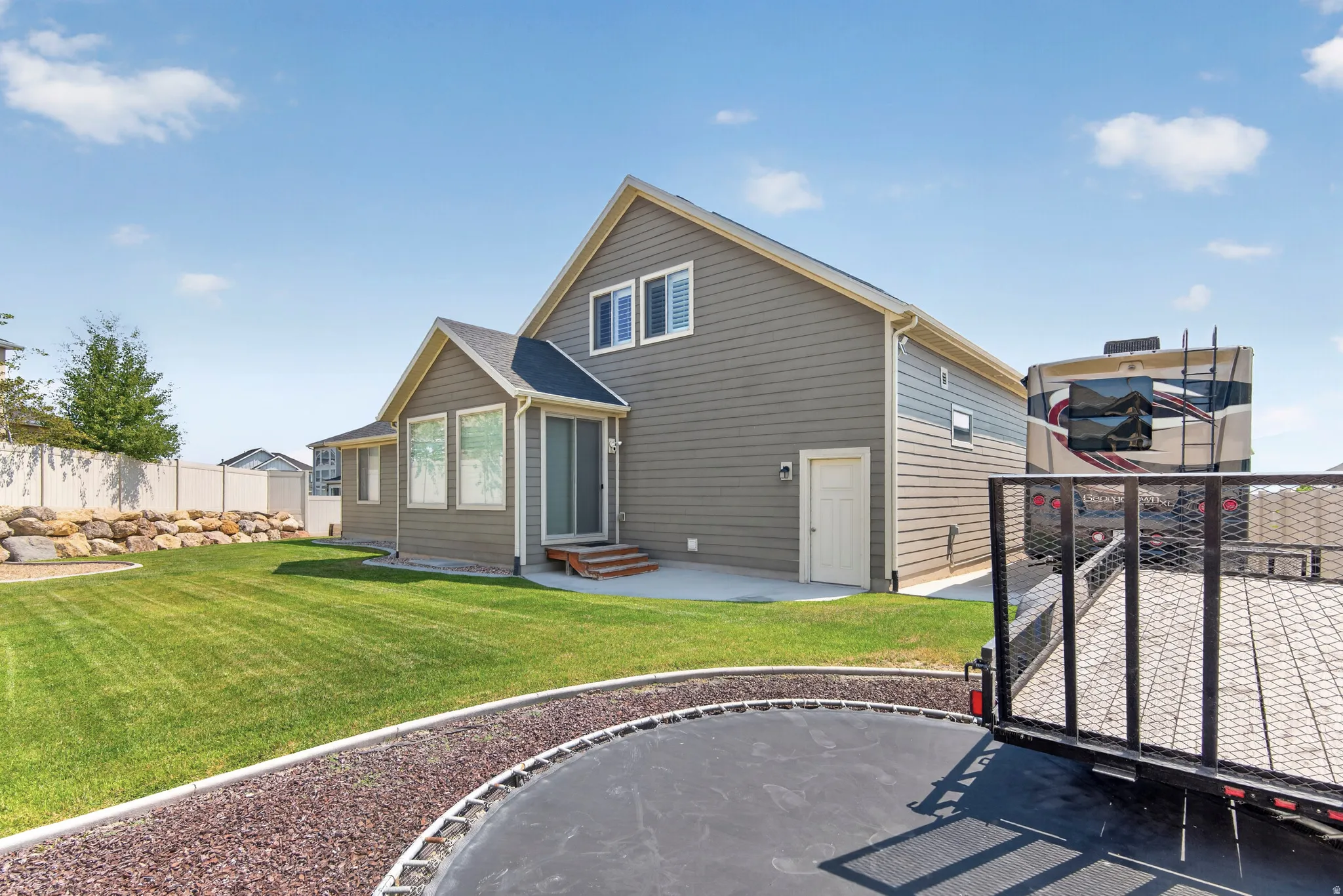 Spacious backyard featuring a manicured lawn, rock retaining wall, and white vinyl fencing