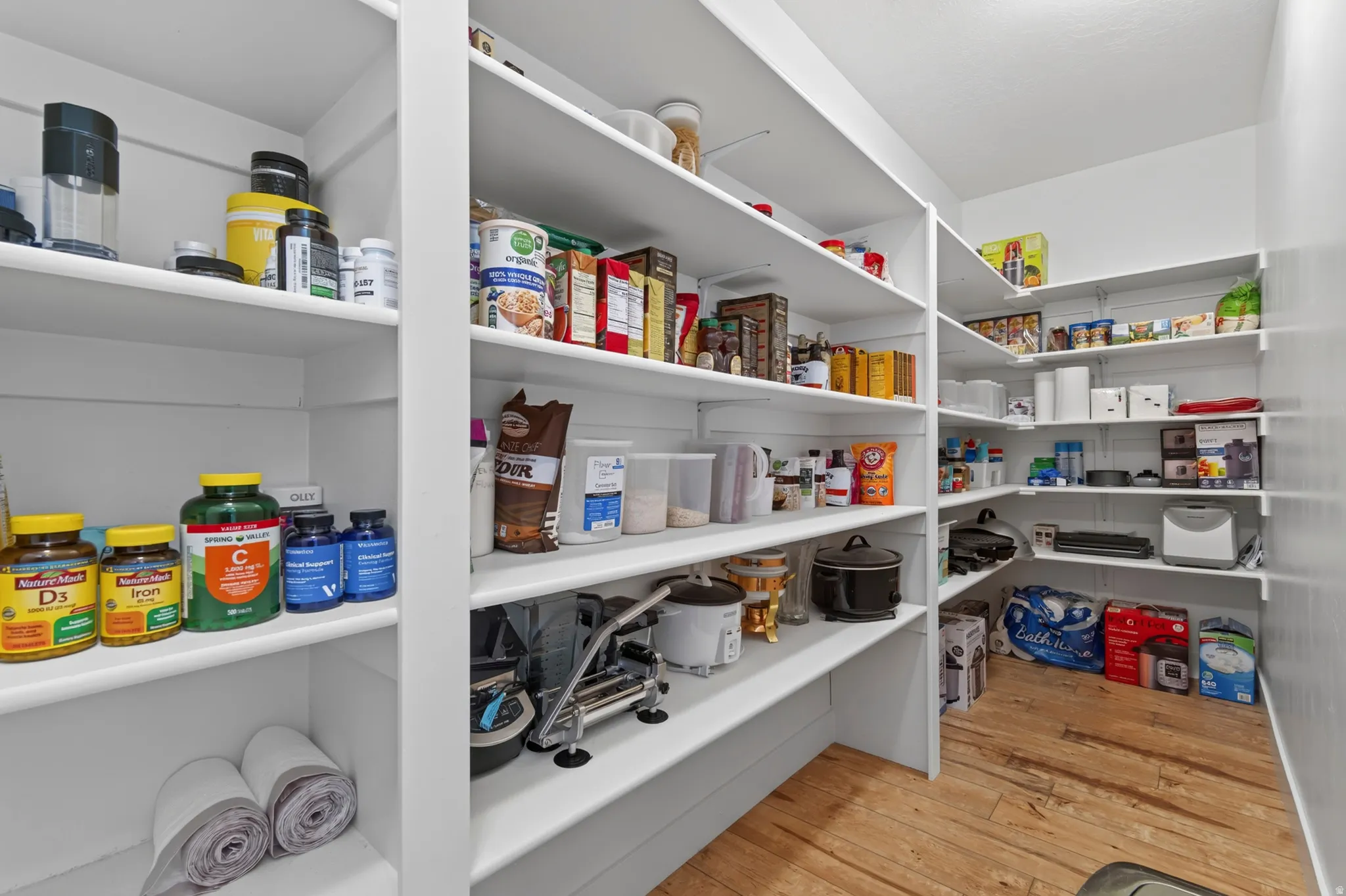 Spacious walk-in pantry featuring extensive white shelving, recessed lighting, and wood-finish flooring
