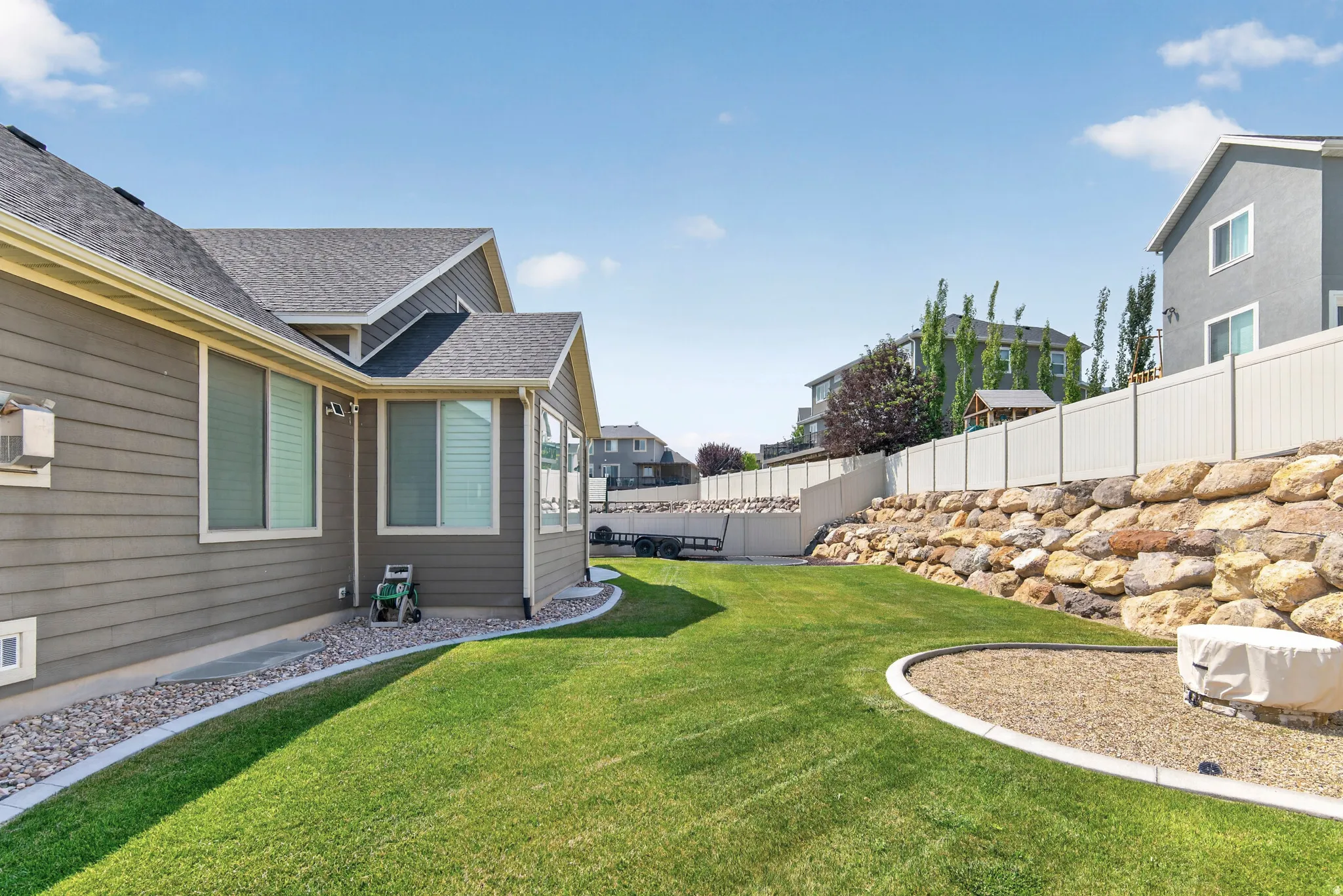 Spacious backyard featuring a sloped lawn, a gravel fire pit area, and a rock retaining wall