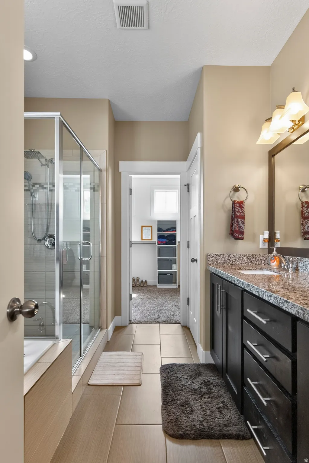 Full bathroom featuring a shower with a clear glass enclosure, a built-in bathtub, tile flooring, and a dark wood-finish vanity with a light-colored countertop