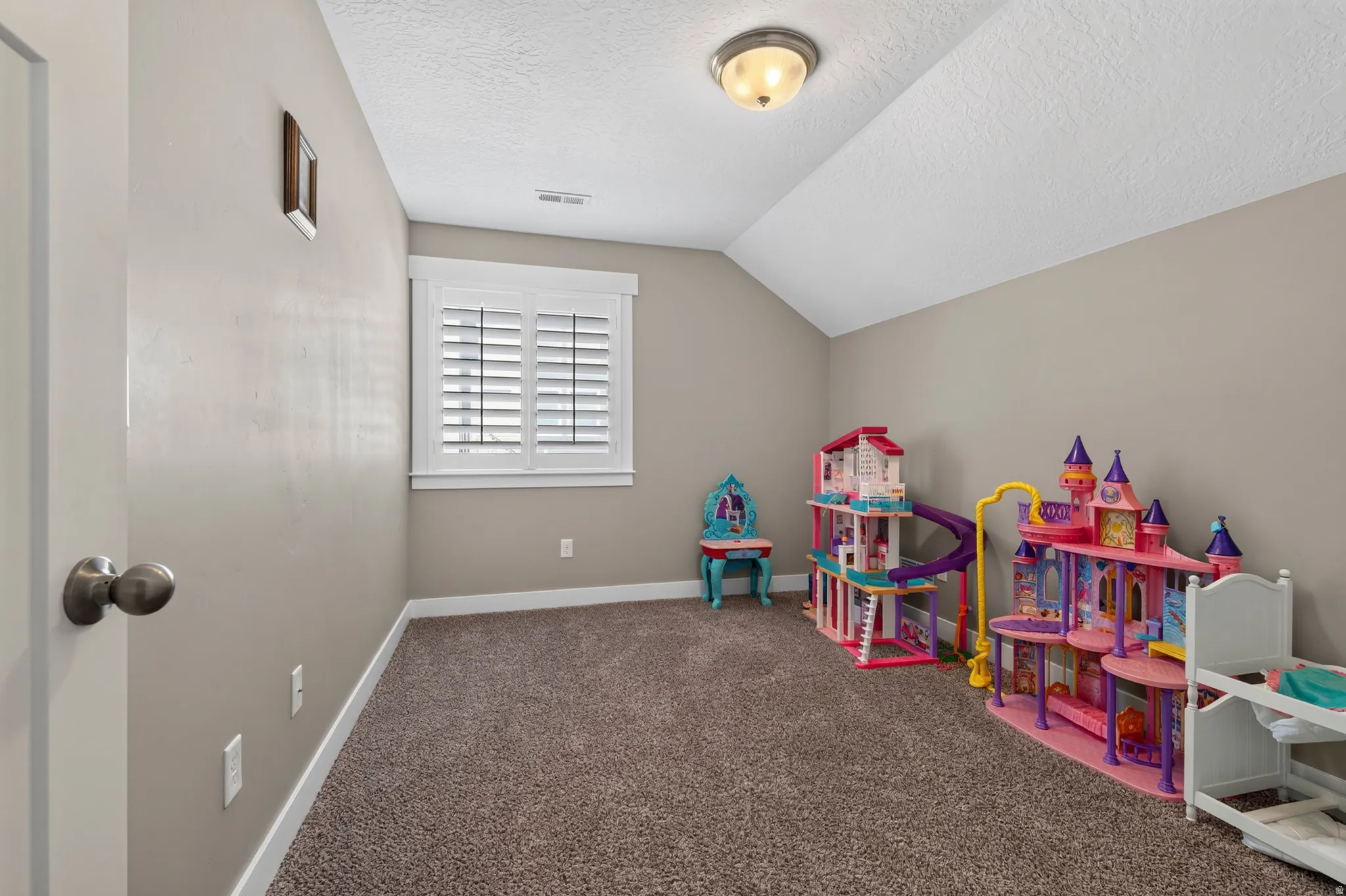 Carpeted room with a vaulted ceiling and neutral wall paint