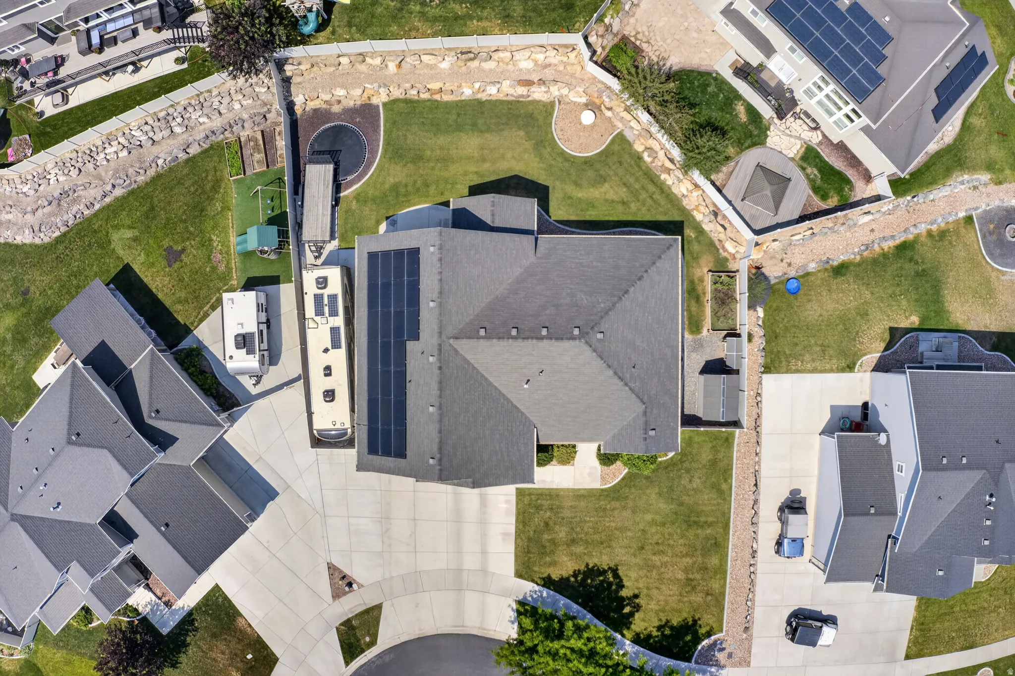 Property featuring an expansive driveway and a multi-pitched roof with solar panels