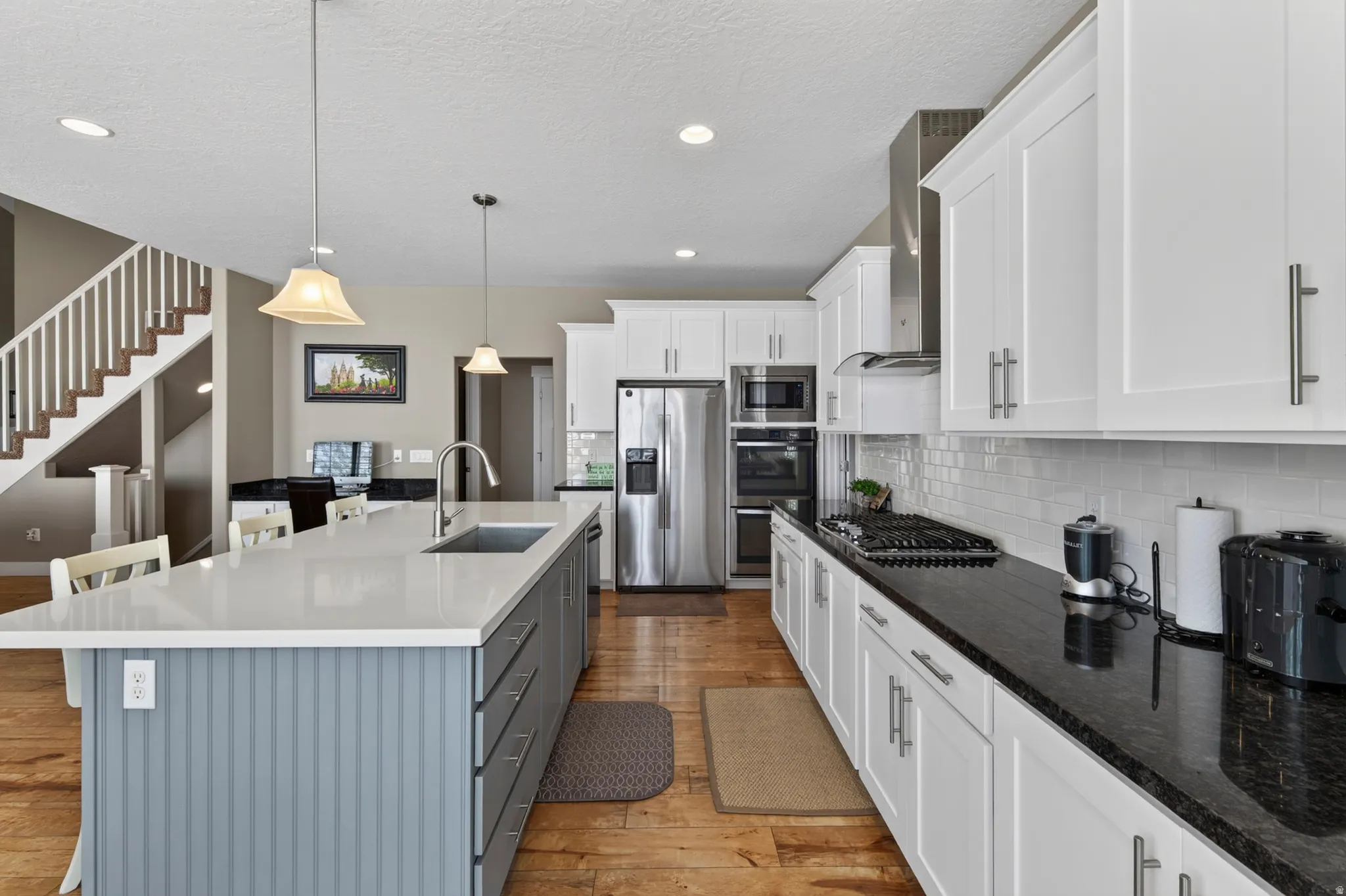 Spacious kitchen featuring an expansive center island with a light-toned countertop and beadboard paneling, white shaker cabinetry with brushed nickel hardware, and stainless steel appliances