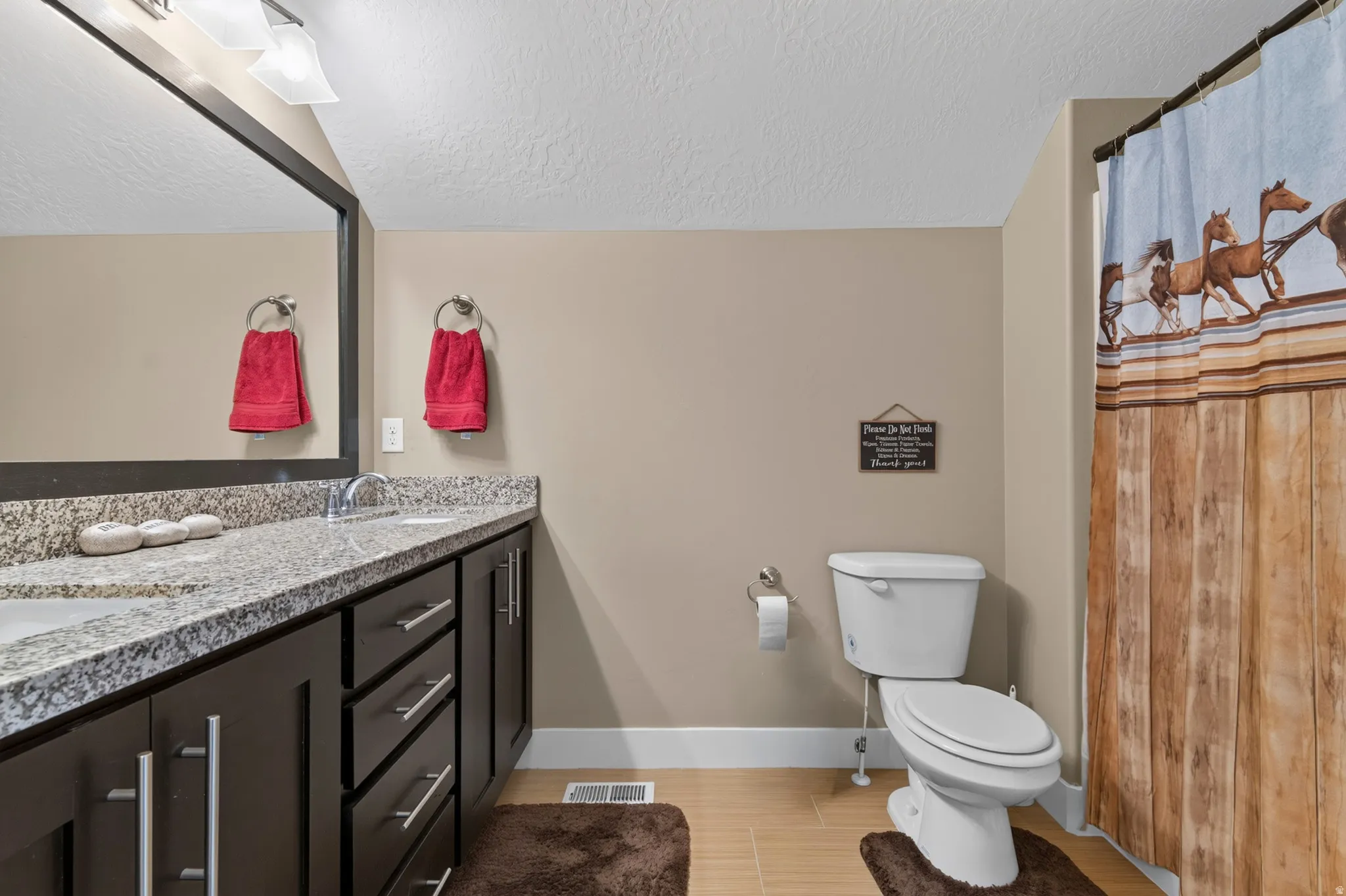 Bathroom featuring a double vanity with a speckled countertop, dark wood-finish cabinetry, and a framed mirror