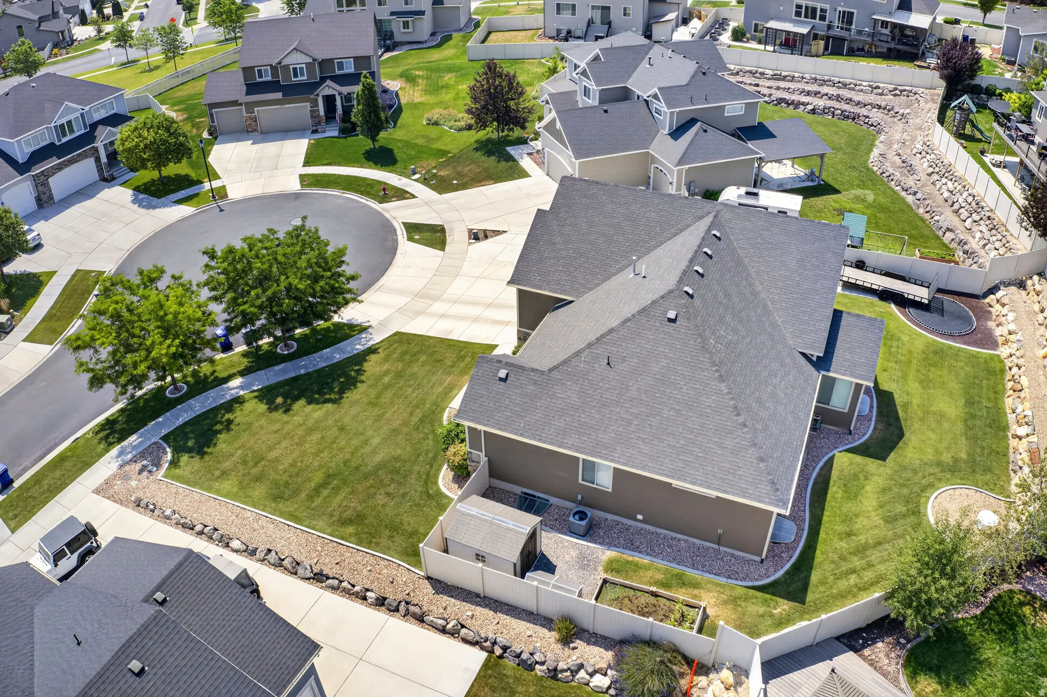 Overhead view of a suburban neighborhood featuring a residential property with a dark shingle roof, tan siding, and a white privacy fence
