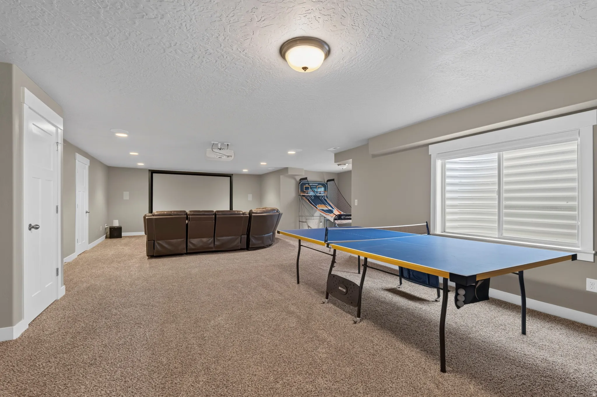 Expansive finished basement featuring recessed lighting, a large projection screen, and a window with blinds