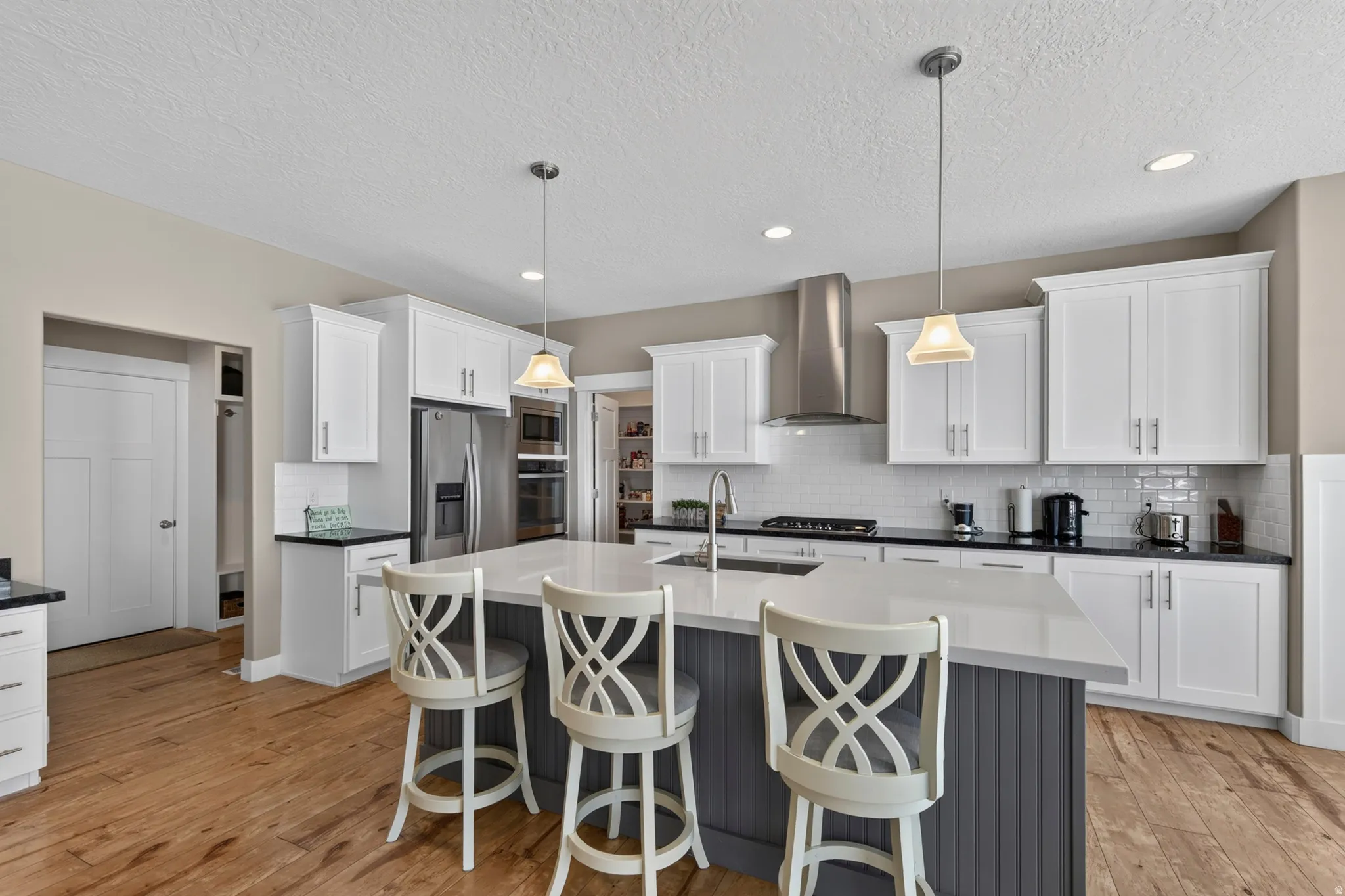Kitchen featuring wood-finish flooring, white cabinetry, stainless steel appliances, a center island with pendant lighting, and a subway tile backsplash