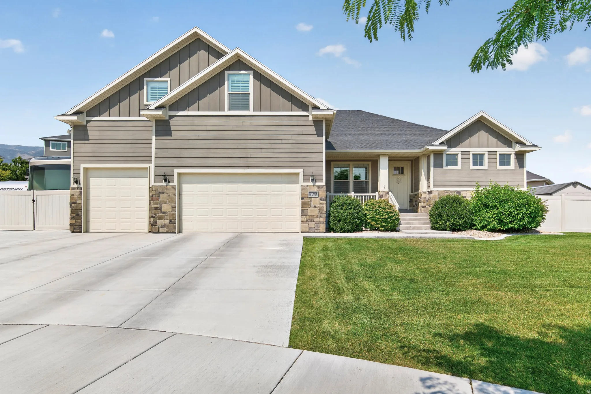 Exterior featuring horizontal siding, stone accents, a multi-car driveway, a covered porch entry, and a manicured lawn