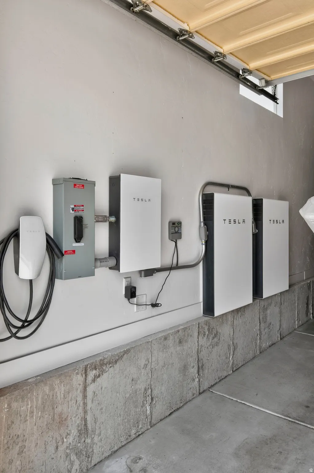 Integrated Tesla Powerwall system with three battery units, a Tesla Wall Connector, and electrical panel in a garage setting