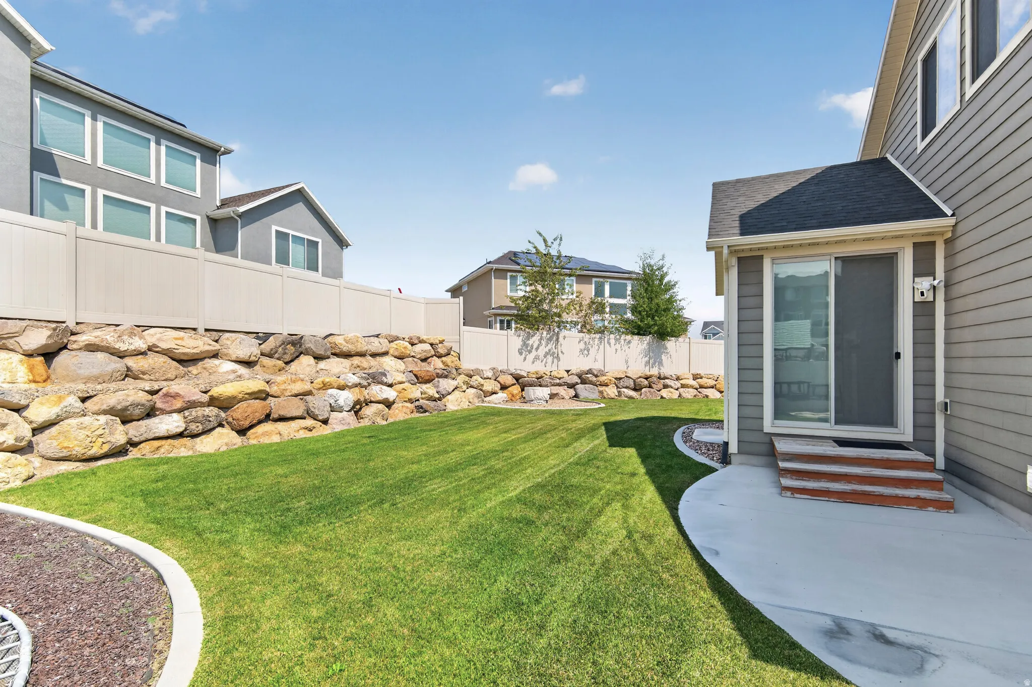 Expansive green lawn with a rock retaining wall and a privacy fence