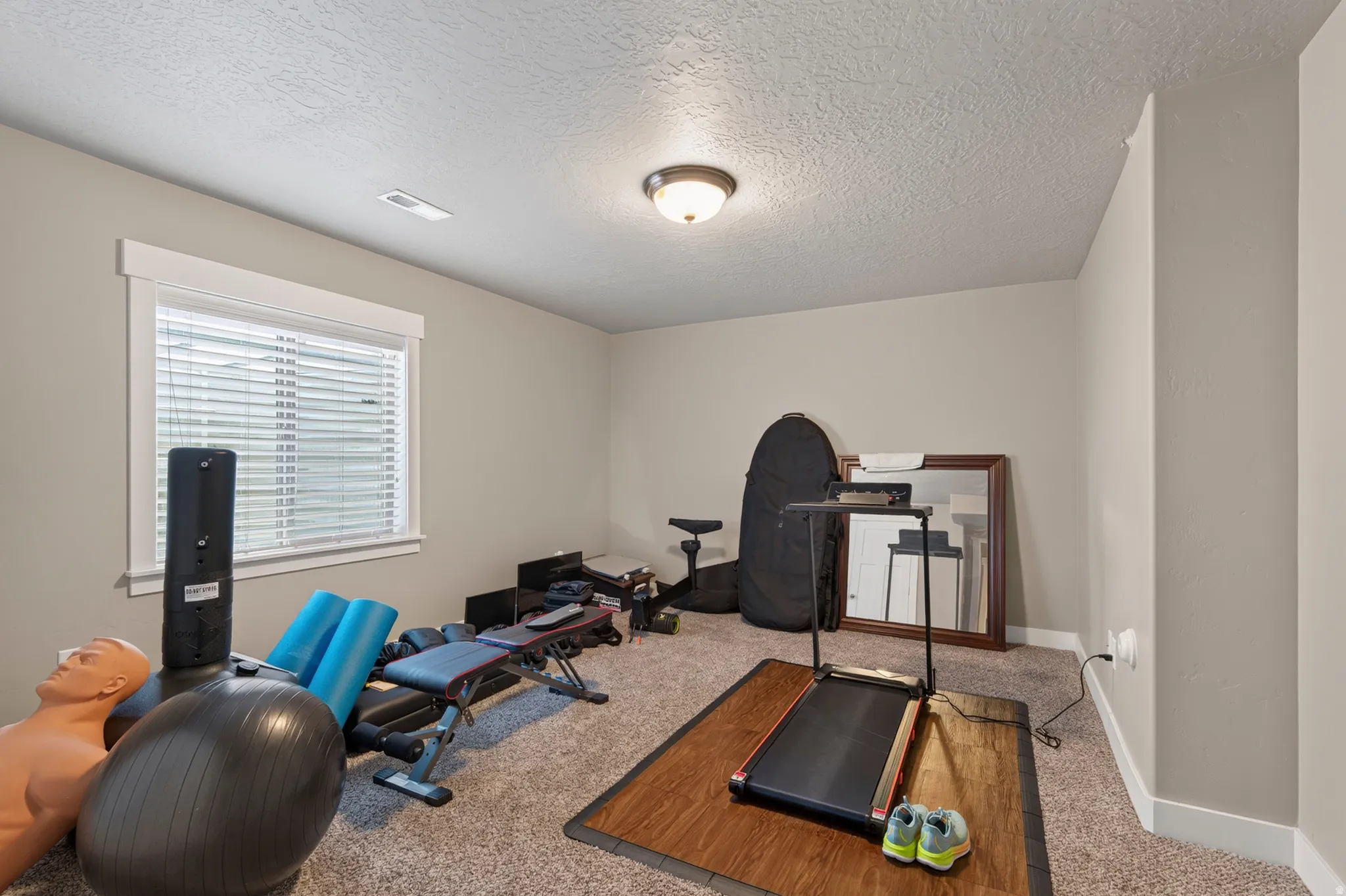 Spacious room featuring neutral painted walls, textured ceiling, and a single window with blinds