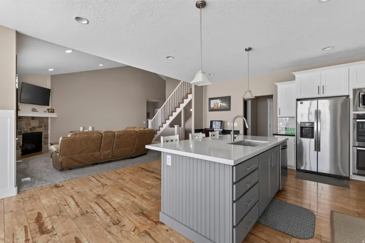 Open-concept kitchen and living area featuring a central island with sink, stainless steel appliances, wood-finish flooring, and a stone-faced fireplace