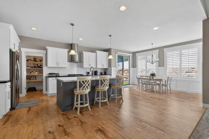 Open-concept kitchen and dining area featuring wide plank wood-finish flooring, white shaker cabinetry, a central island with bar seating, and a walk-in pantry