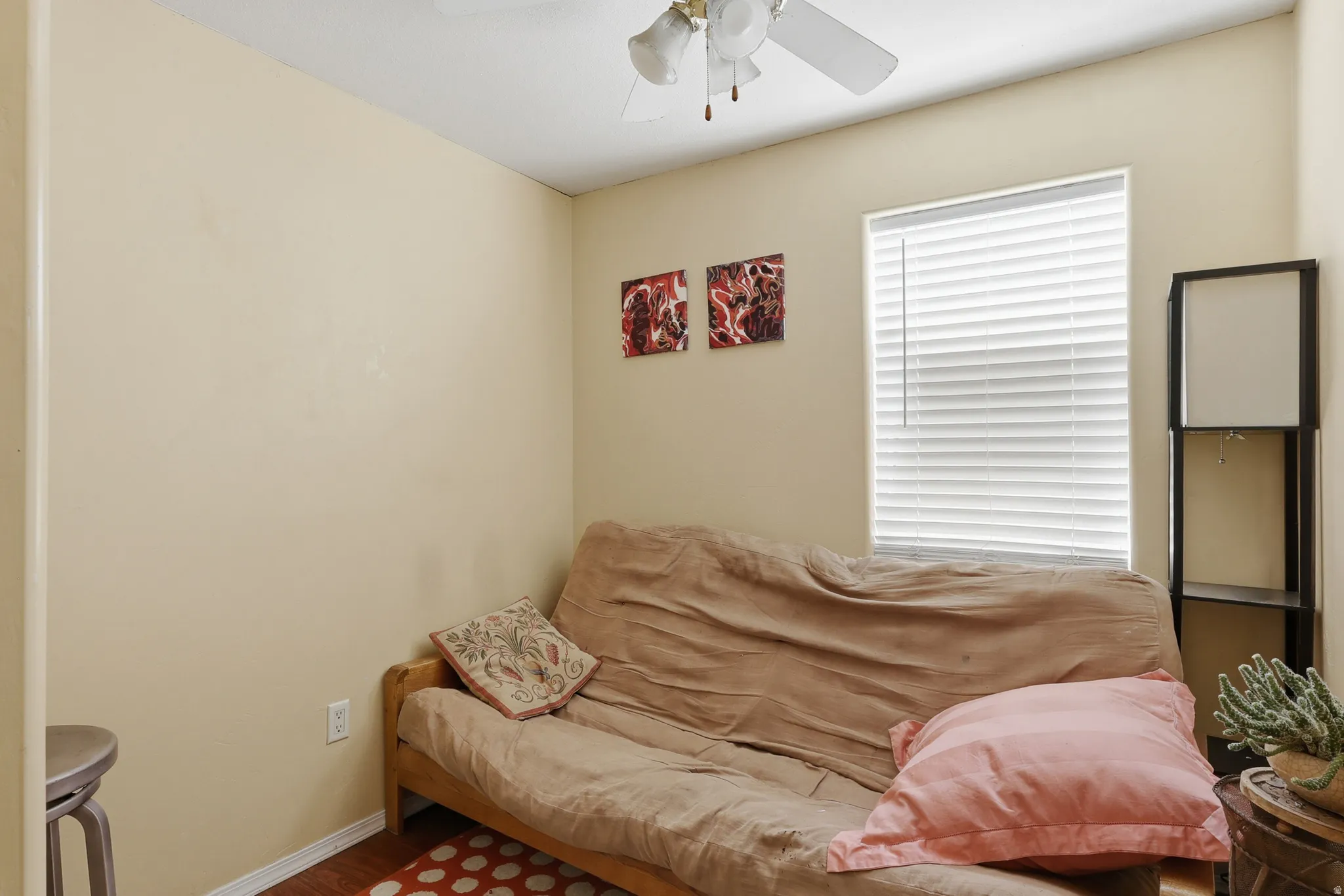 Compact room featuring a window with horizontal blinds, wood-finish flooring, a ceiling fan, and neutral-toned walls