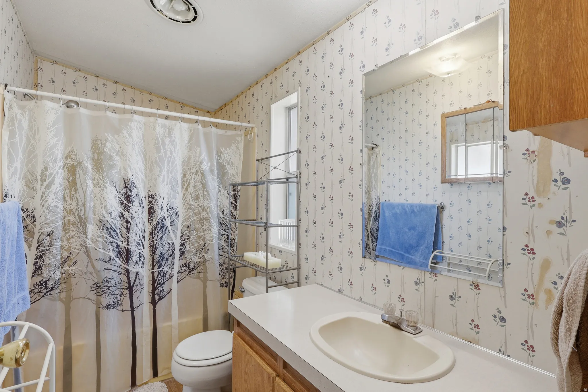 Bathroom featuring a vanity with a white countertop and oval sink, a wall-mounted mirror, and a shower-over-tub combination with a white shower curtain rod