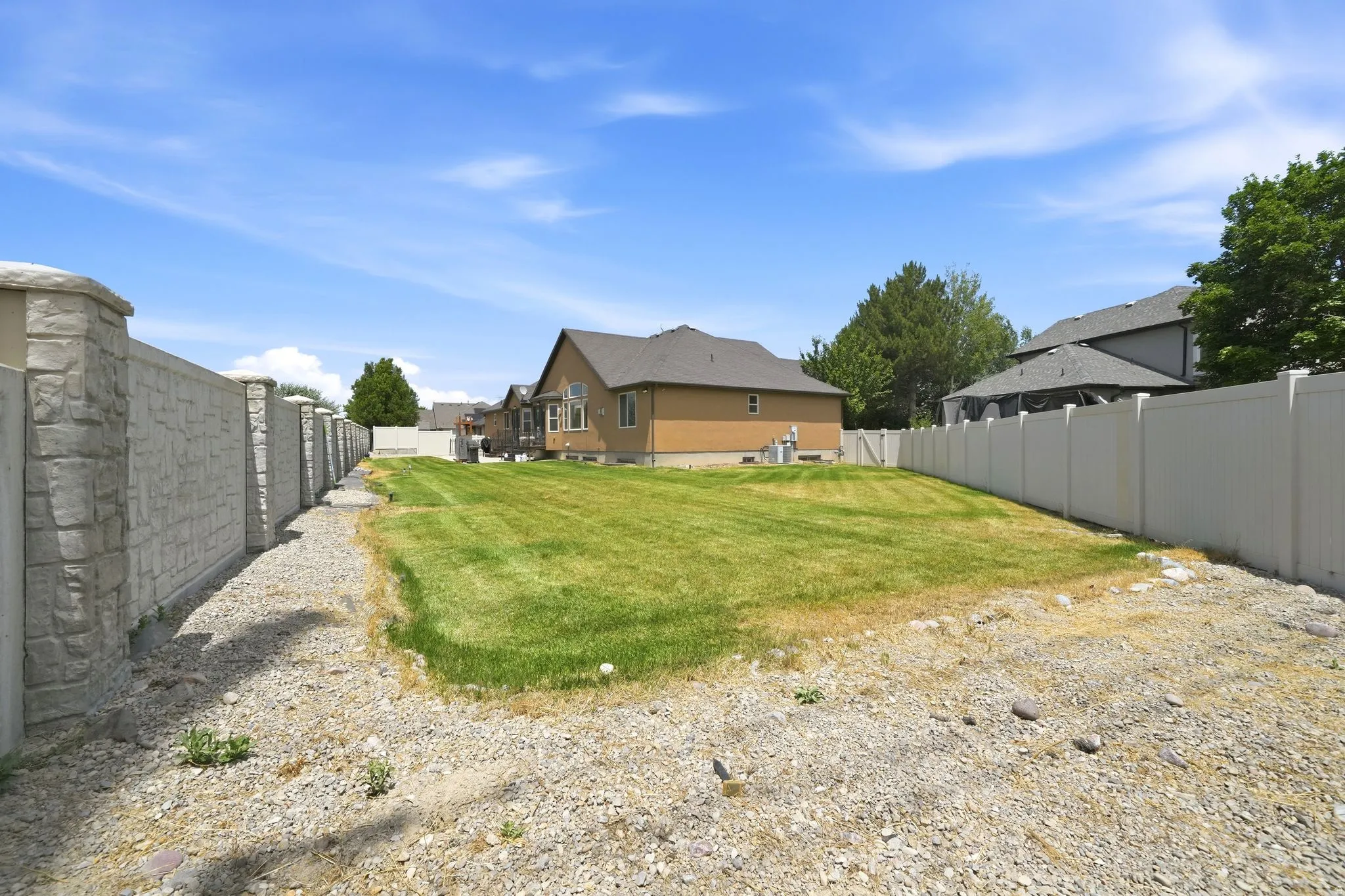 Spacious outdoor area featuring a manicured lawn, stone-finish privacy fencing, and a vinyl privacy fence