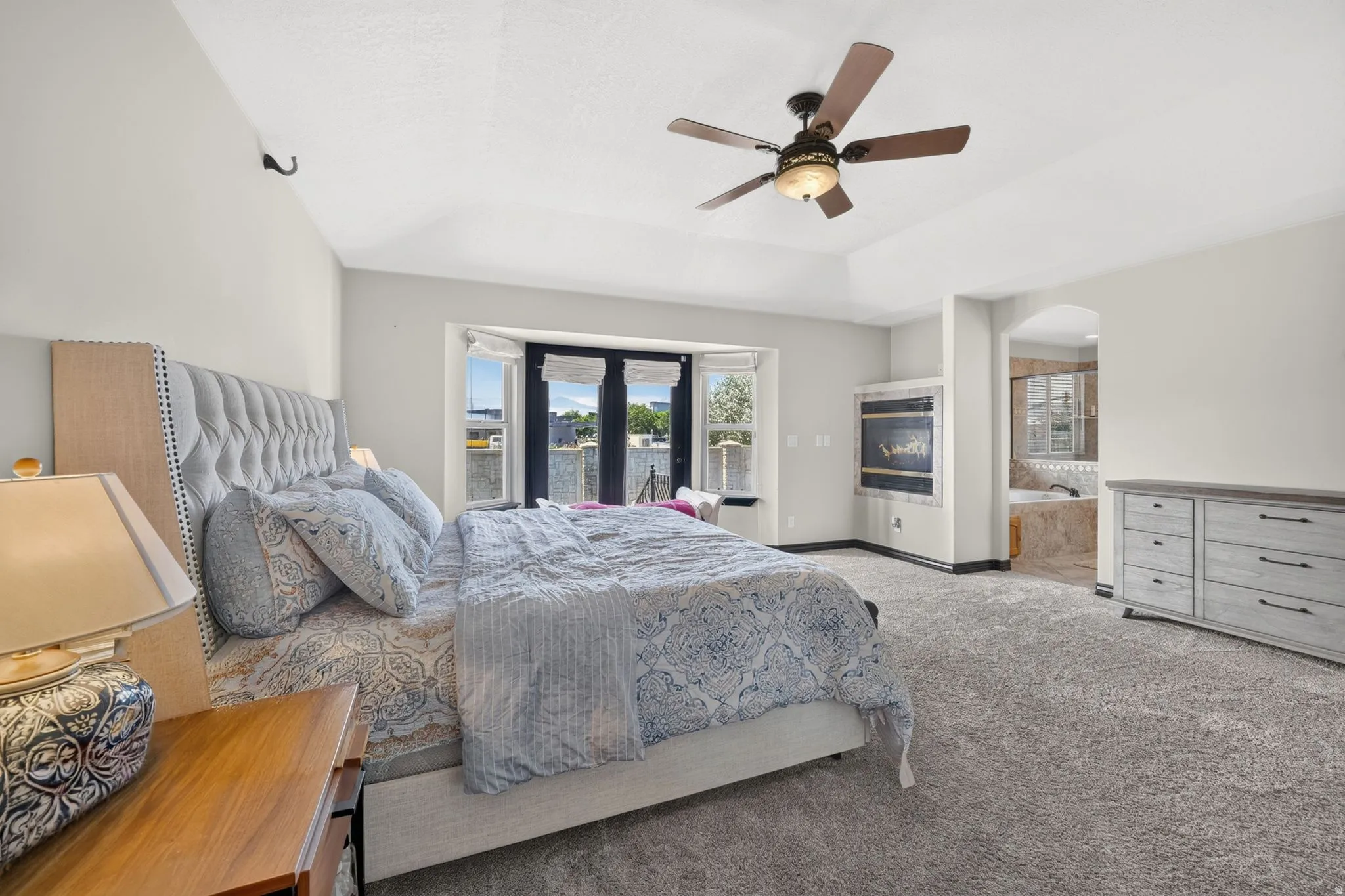 Primary bedroom with Tray ceiling bedroom featuring a ceiling fan, recessed wrap around fireplace, and french doors & bay window with water views