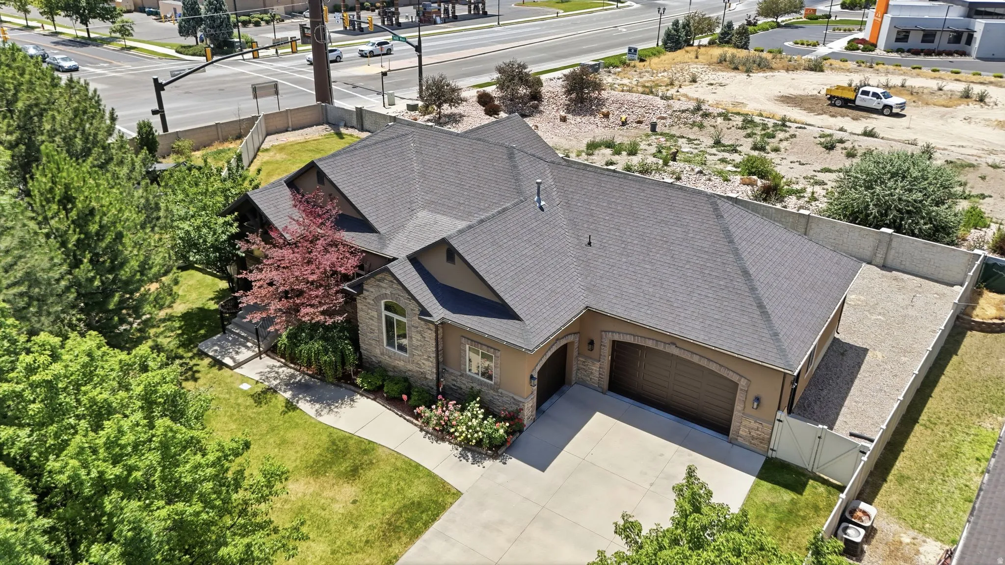 Stucco and stone exterior featuring a dark asphalt shingle roof, arched garage doors, a concrete driveway, and mature landscaping