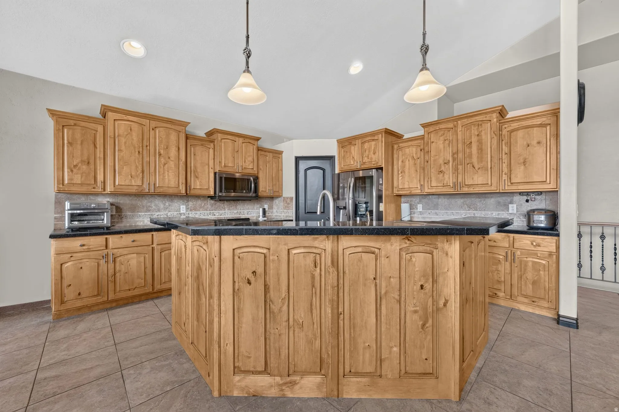 Kitchen featuring extensive wood cabinetry, a large central island with a sink, dark countertops, tiled flooring, and recessed lighting