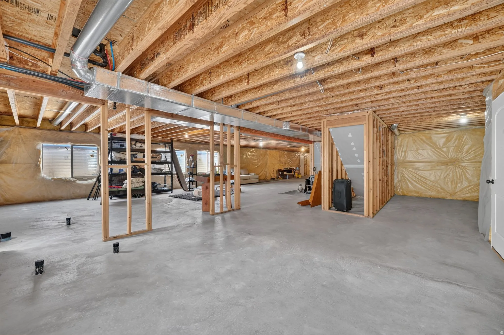 Unfinished basement featuring exposed wood joists, concrete flooring, framed interior walls, and visible ductwork
