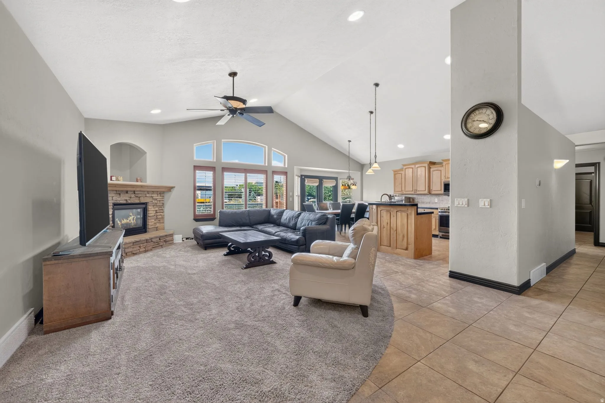 Vaulted ceiling living area featuring a stone-faced fireplace, large windows, recessed lighting, and a ceiling fan