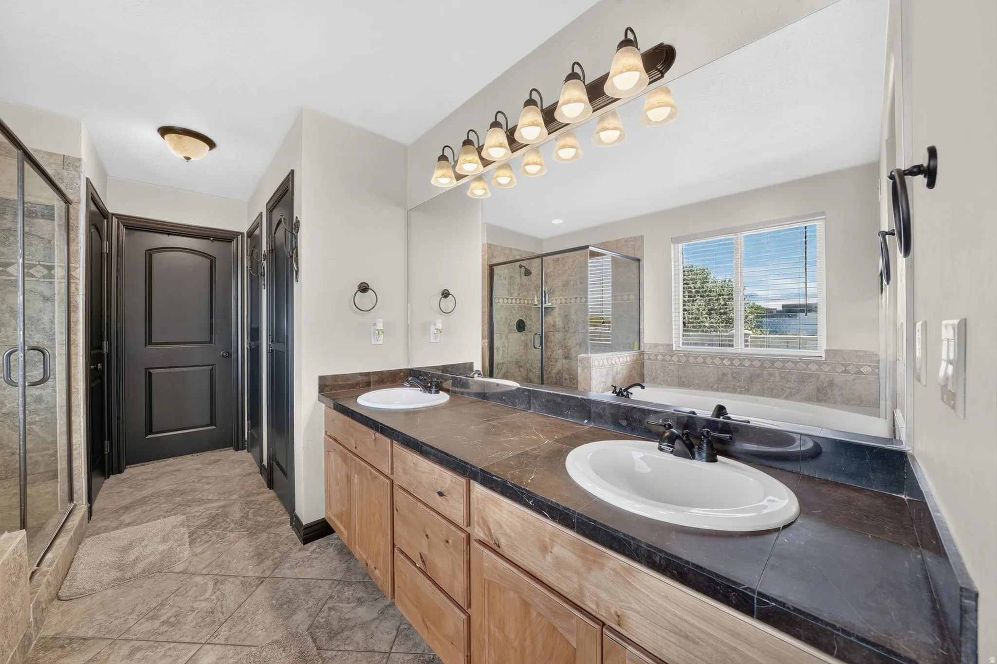 Primary Bathroom featuring a dual vanity with sinks, a large mirror, a separate shower enclosure, and a built-in bathtub with tiled surround