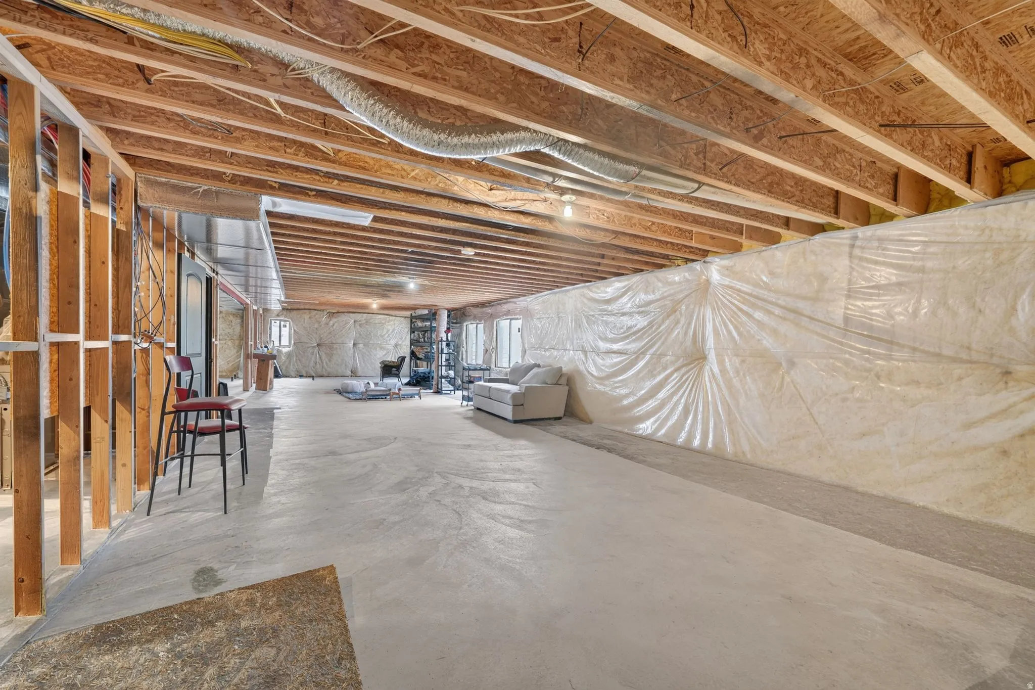 Unfinished lower level featuring exposed wood joists and subfloor, concrete flooring, and framed wall sections