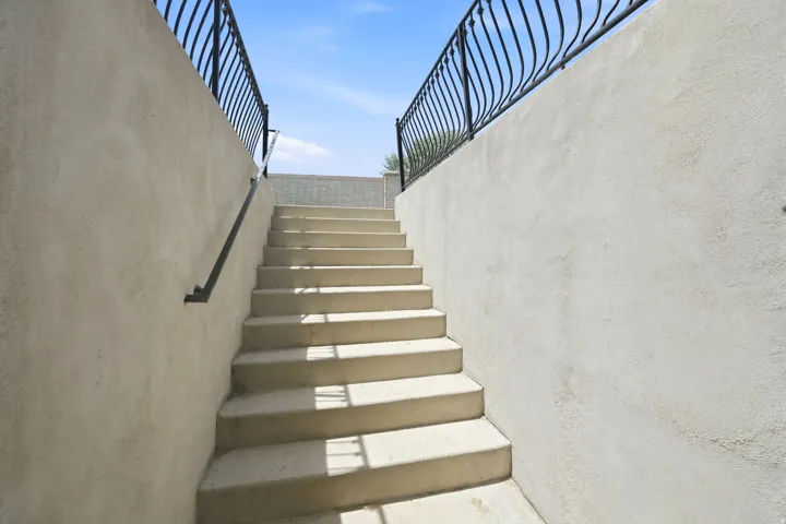 Concrete exterior staircase featuring stucco walls and wrought iron railings