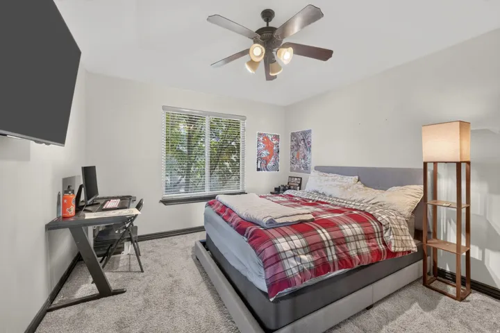 Carpeted Second bedroom featuring a ceiling fan with integrated lighting, a window with blinds, and a built-in wall-mounted television