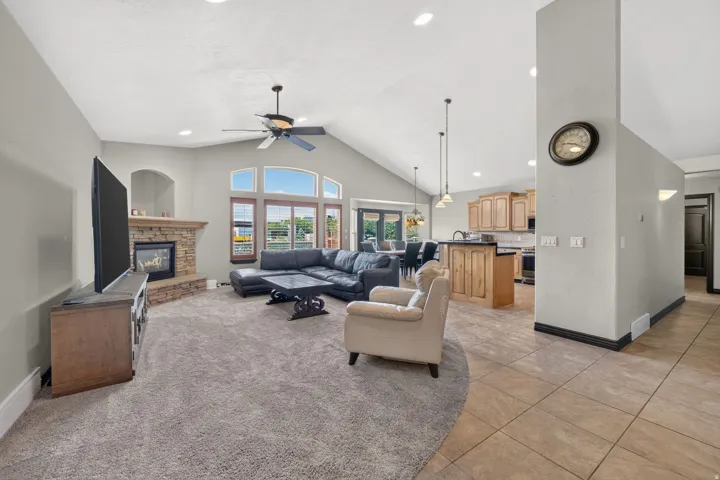 Vaulted ceiling living area featuring a stone-faced fireplace, large windows, recessed lighting, and a ceiling fan
