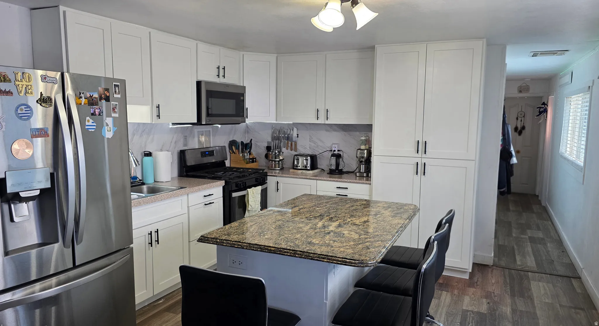 Kitchen featuring an island with a stone countertop, white shaker cabinetry, stainless steel appliances, and wood-finish flooring