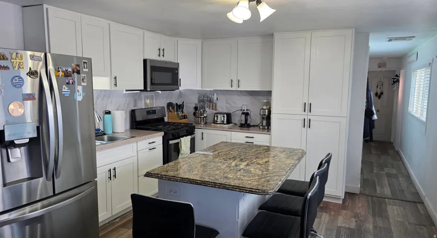 Kitchen featuring an island with a stone countertop, white shaker cabinetry, stainless steel appliances, and wood-finish flooring