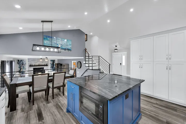 Kitchen island with beautiful granite countertops and built-in microwave, upgraded NuCore performance ridged-core LVP flooring,, white cabinetry, and a modern linear light fixture