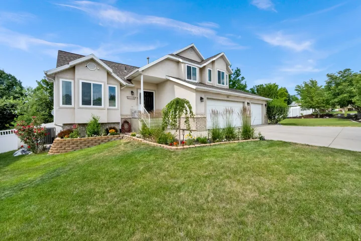 Stucco exterior with stone accents, featuring a two-car garage, concrete driveway, and front landscaping with a retaining wall