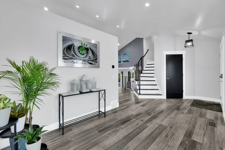 Entryway featuring upgraded NuCore performance ridged-core LVP flooring, a modern custom staircase with metal railings, a black panel door, a contemporary hanging light fixture, and recessed lighting