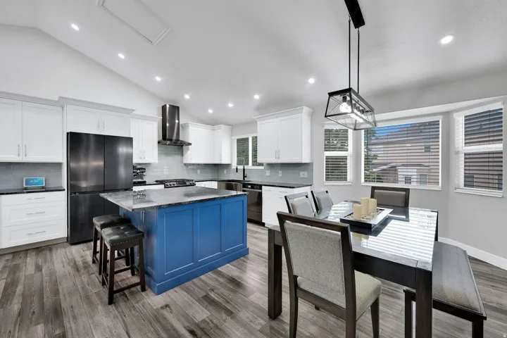 Kitchen featuring a blue island with seating, beautiful granite countertops, custom white cabinets, and black stainless steel appliances