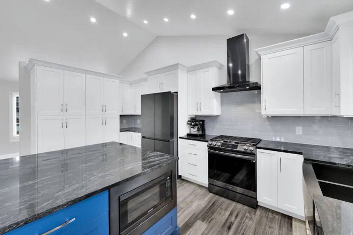 Kitchen featuring a large island with a built-in microwave, white shaker cabinetry, beautiful granite countertops, a black range with a matching range hood, and upgraded flooring