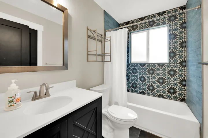 Bathroom featuring a white bathtub, patterned tile surround, and a white vanity with an undermount sink