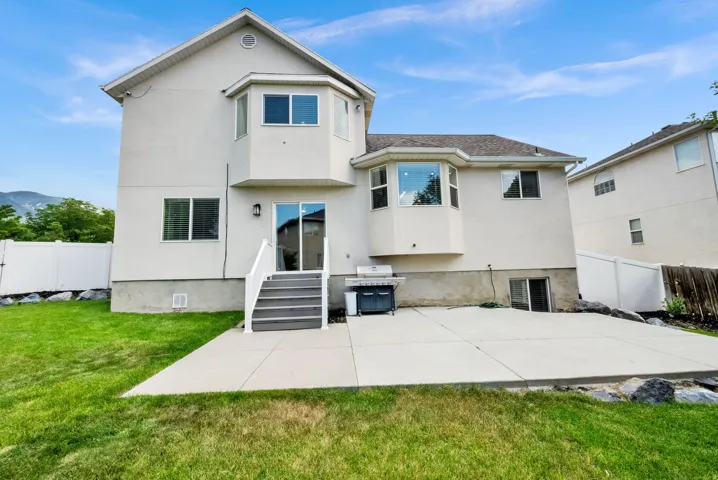 Spacious backyard featuring a large concrete patio, expansive lawn, and white privacy fencing