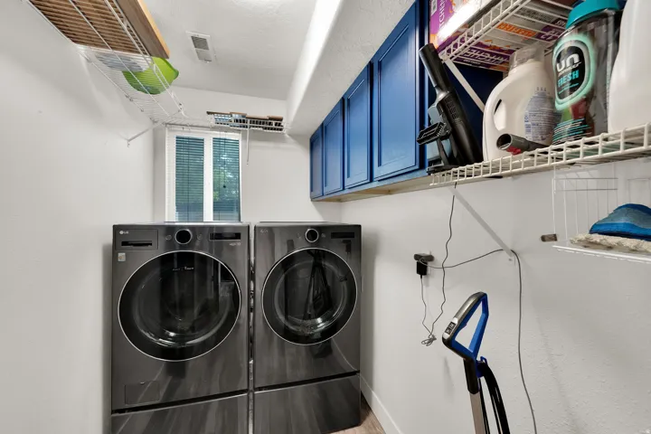 Dedicated laundry area featuring a window with blinds, blue upper cabinetry, white wire shelving, and upgraded flooring
