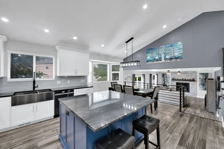 Kitchen featuring an oversized island with built-in storage, granite countertops, white custom shaker cabinetry, black stainless steel farm sink and upgraded NuCore performance ridged-core LVP flooring,