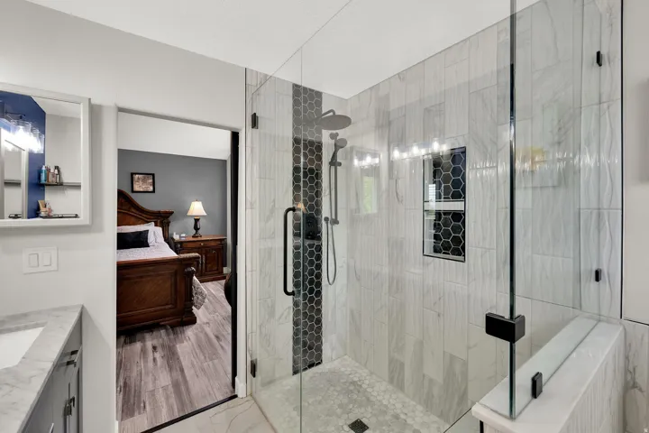 Glass-enclosed shower with a rainfall showerhead, handheld shower fixture, and a built-in recessed shelf with hexagonal tile