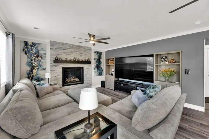 Living area featuring a stone-clad fireplace with a dark wood mantle, upgraded NuCore performance ridged-core LVP flooring,, and crown molding