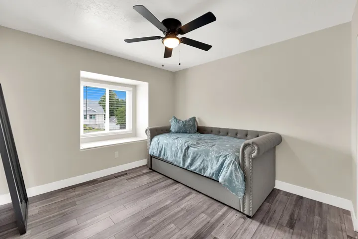 Room featuring wood-finish flooring, a window with blinds and a deep sill, neutral wall paint, white trim, and a ceiling fan with integrated lighting