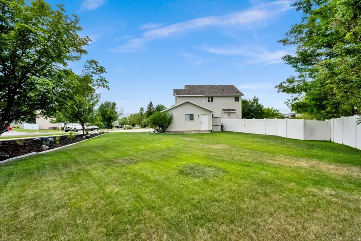 Expansive lawn area featuring a white privacy fence, mature trees, and a raised landscaping bed with dark mulch