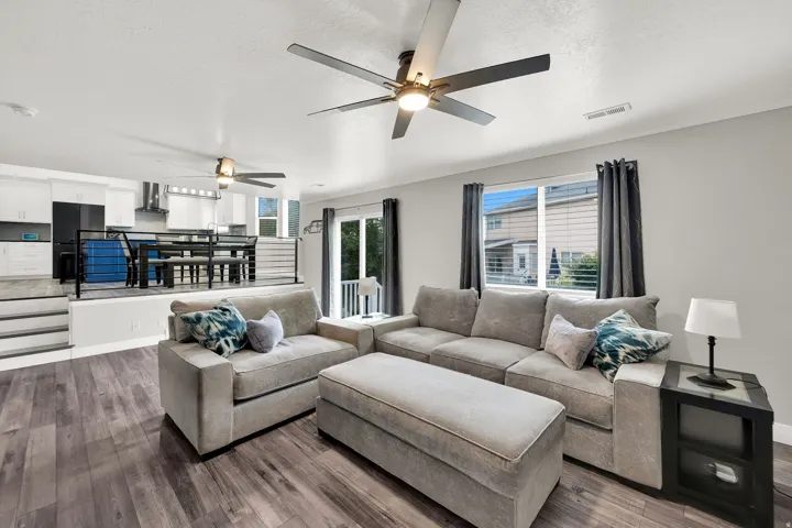 Spacious living area featuring upgraded flooring, two ceiling fans with integrated lighting, and a sliding glass door leading to an outdoor space