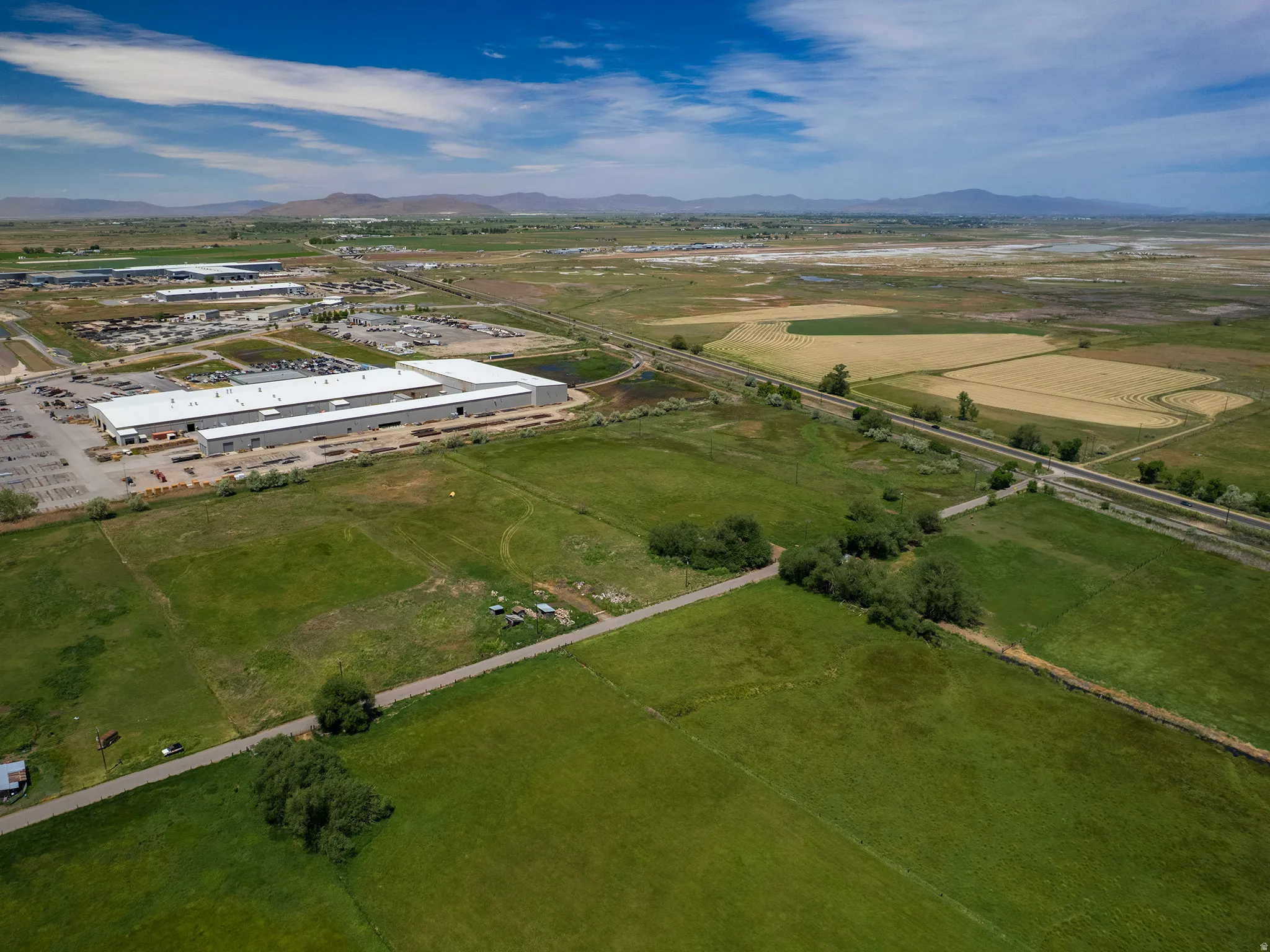 Expansive green fields featuring distant industrial buildings, agricultural land, and a visible railway line