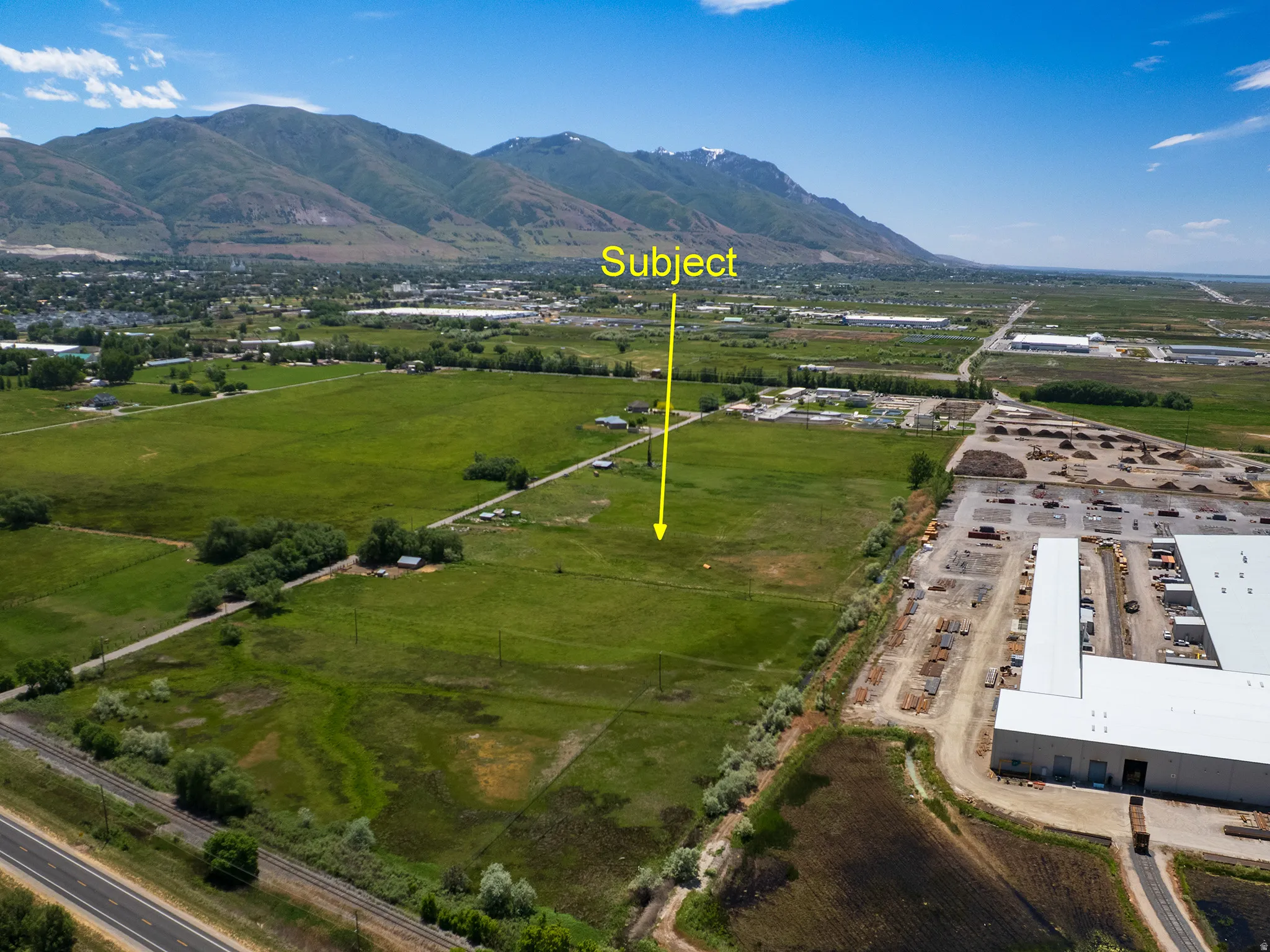 Expansive undeveloped land featuring a green field, distant mountainous terrain, and clear skies