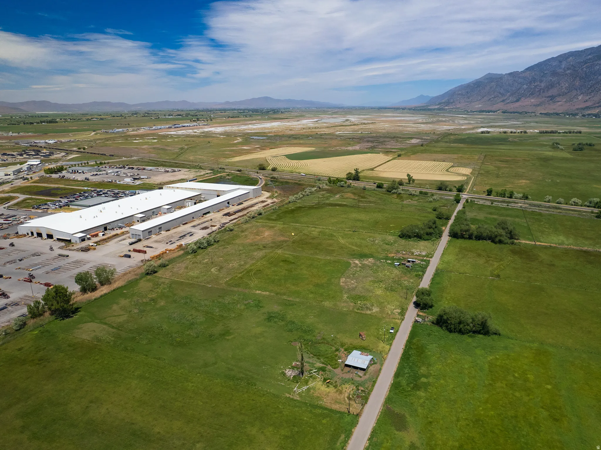 Expansive green acreage featuring a paved road, agricultural fields, and distant mountains